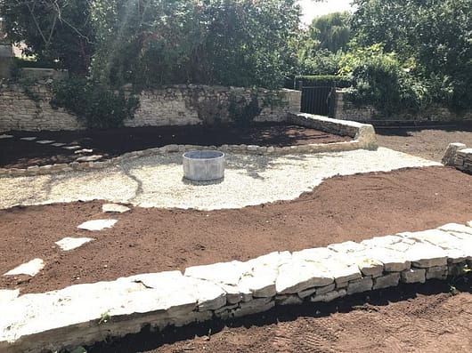 A newly built kitchen garden located in the sun with freshly prepped topsoil and cotswold stone